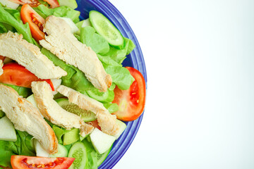 Salad with difference lettuce tomato and baked chicken breast on blue dish