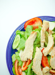Salad with difference lettuce tomato and baked chicken breast on blue dish
