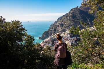 Tourist woman with backpack enjoying panoramic view on colorful houses of coastal town Positano, Amalfi Coast, Italy, Campania, Europe. Vacation at coastline at Mediterranean Sea. Path of the Gods