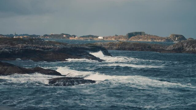 Powerful waves are crashing on the rocky shores near the Atlantic road, in Norway. Seagulls fly above the water. Slow-motion, pan left.