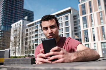 Young man sitting on a bench using his mobile phone in an urban environment.