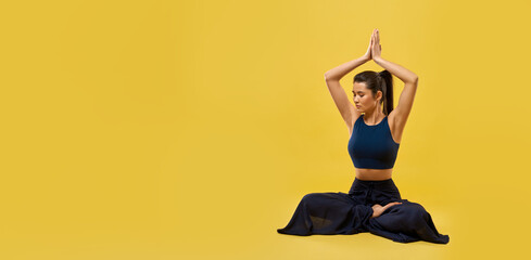 Panorama of brunette girl practicing yoga pose at studio. Slim young woman sitting on floor, holding prayer hands above head, looking down. Concept of new age and yoga doing, - obrazy, fototapety, plakaty
