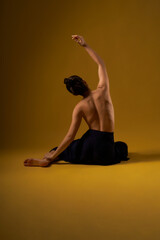 Back view of flexible girl with bare back sitting backwards on floor, with raised hand. Brunette...