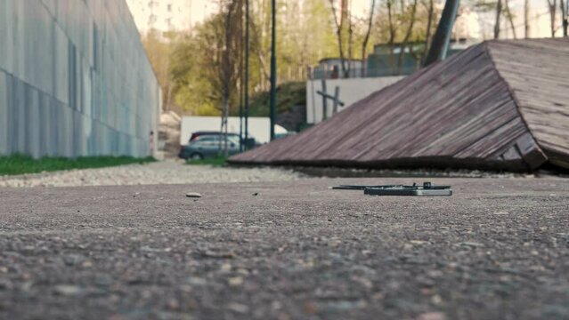 A small silver mobile phone falls from a height to the asphalt, breaks in slow motion and shatters into pieces on the ground. A sunny summer day in the parking lot of a residential building. Close up.