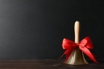 Golden bell with red bow on wooden table near blackboard, space for text. School days
