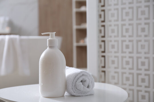 Bottle of shower gel and fresh towel on white table in bathroom. Space for text