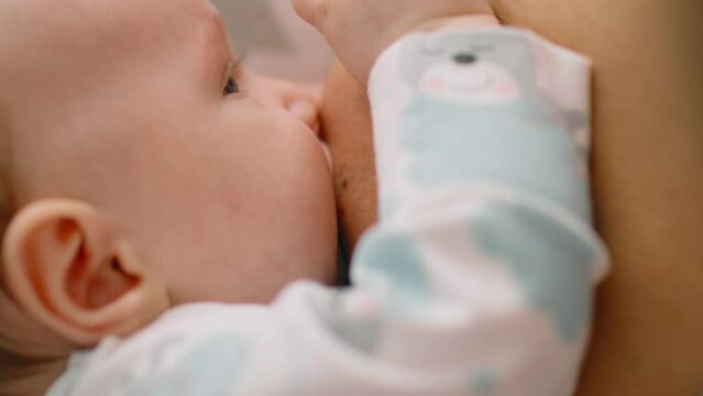 Infant sucks the mother's breast, close-up. Baby is resting and relaxing, enjoying sucking the mother's breast. Natural feeding of the child. Healthy food for a child. Motherhood and child care.