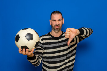 Handsome latin man holding football with angry face, negative sign showing dislike with thumbs down, rejection concept. Isolated on blue background.