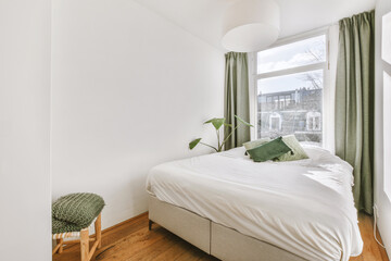 Comfortable bed and chair placed in small narrow minimalist style bedroom with white walls and...