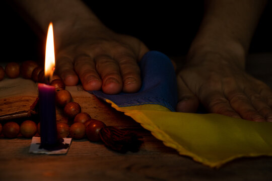Women's hands hold the flag of Ukraine and pray near the candle for the country in the dark, stop the war in Ukraine - Powered by Adobe