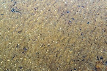 Sand and stones under water background texture. Ground of a lake with clear water on top. Abstract backdrop pattern in a natural area. Pebbles on the sea bottom.