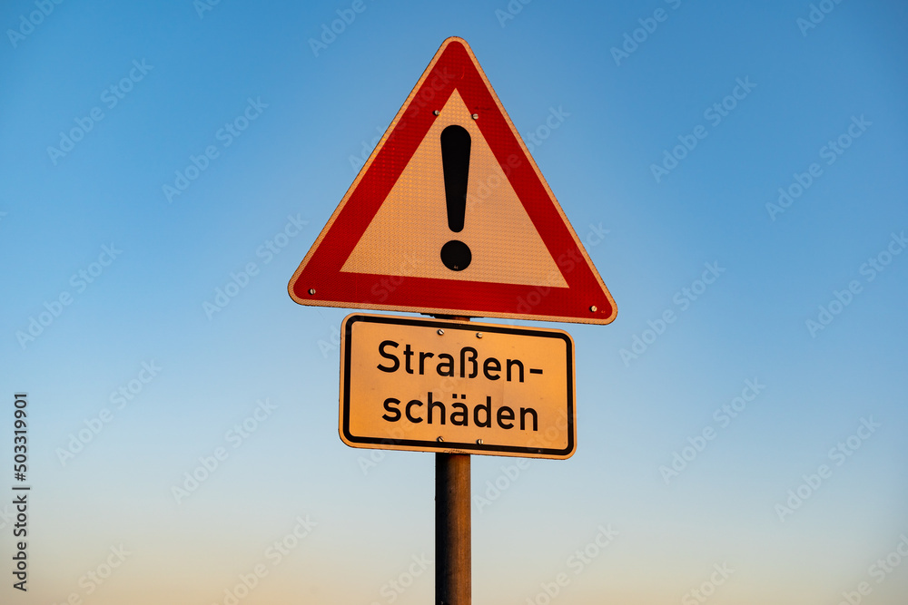 Wall mural Road sign with a warning against road damages. In German language it says 'Straßenschäden' which should slow down the traffic because of a bumpy road. A big exclamation mark is on the symbol.