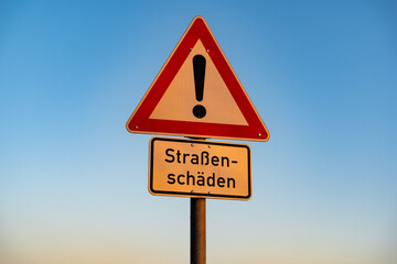 Road sign with a warning against road damages. In German language it says 'Straßenschäden' which...