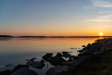 Landscape with the lake Müritz and a beautiful sunset. Reflections in the water and stones in the foreground. Nature in a rural area in Germany. The sky is blue and clear.