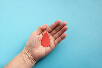 The concept of the World Blood Donor and Hemophilia Day. Red paper drop of blood in the hand on a...