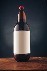 Brown plastic bottle of beer, ale or kvas with blank label, no brand on dark wooden background. Alcohol drink advertising, mockup