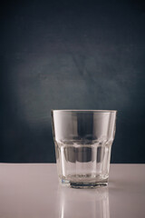 Empty transparent glass on white table, dark backdrop. Glassware. Copy space, vertical shot