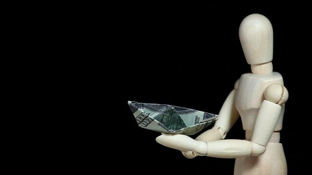 footage of wooden mannequin origami money boat dark background 