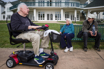 Solomons, Maryland  A senior man sits outdoors on an electric wheelchair and chats with his wife and grandson. - obrazy, fototapety, plakaty