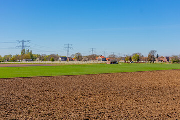 Fototapeta na wymiar Farmland prepared for cultivation, uncultivated and cultivated, fruit trees, white flowers, farmhouses and high-voltage pylons in the background, sunny day in Stevensweert, South Limburg, Netherlands