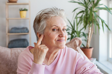 senior woman pointing finger at her ear, looking at camera and smiling