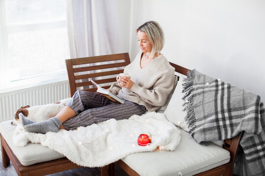 Adult 40s woman is reading a book in living room at cozy home