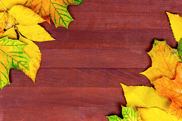 Naklejka na ściany i meble Bright colorful yellow and orange autumnal leaves on brown wooden plank background with copy space top view.