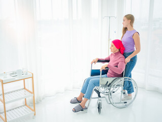 A cancer-stricken mother sits in a wheelchair looking at the evening sun, with her daughter visiting as a wheelchair in a hospital ward.