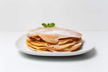 Photo of vegan thin pancakes, on the white plate, decorated with mint leaf.