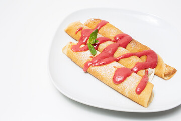 Vegan dessert. Rolled pancakes with strawberry cream topping, on white.