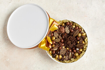 Round box with chocolate sweets in the form of flowers and gold leaves. Top view