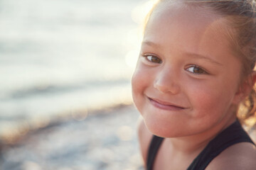 Portrait of a tanned little girl in the rays of the sun against the background of the sea