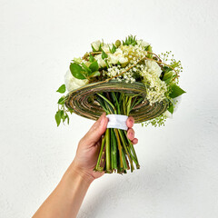Wedding bouquet created on a frame of green branches in a hand of woman