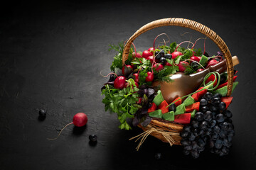 Basket filled with vegetables, cheese, grapes and a bottle of wine on a black background