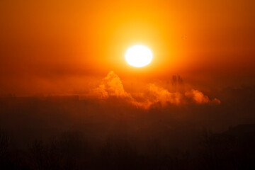 Wonderful, misty morning with sun painting sky orange, creating silhouettes of trees and buildings covered in mist