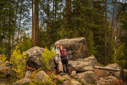 Environmental portrait of senior couple hiking in Rocky Mountains, Colorado, in autumn; rocks, pine trees and distant mountain in background