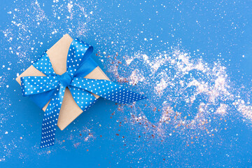 Christmas present box with blue ribbon bow on blue backgrounds with sparkles around. Beautiful Christmas and New Year festive background with copy space. Gift box