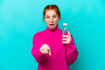 Young caucasian reddish woman with a bottle of water isolated on blue background surprised and pointing front