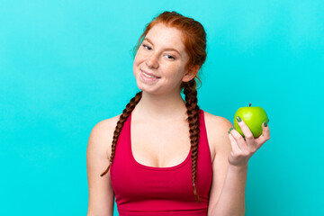 Young reddish woman isolated on blue background with an apple