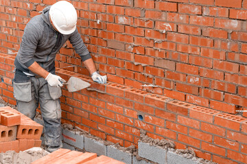 Bricklayer laying bricks on mortar on new residential house construction - obrazy, fototapety, plakaty