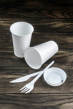 Single-use white plastic items on table. Cups, knife and fork