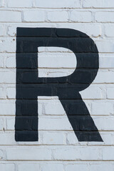Black letter R painted to brick wall on white background (from a letter set containing B, C, D, F, G, M, R and 1, 3, 4)