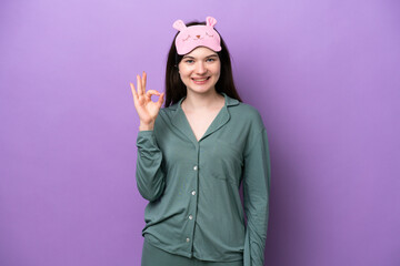 Naklejka premium Young Russian woman in pajamas isolated on purple background showing ok sign with fingers