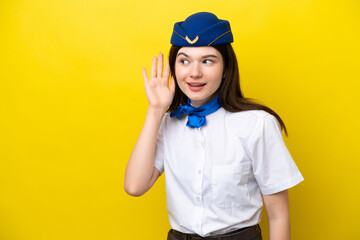 Airplane stewardess Russian woman isolated on yellow background listening to something by putting hand on the ear