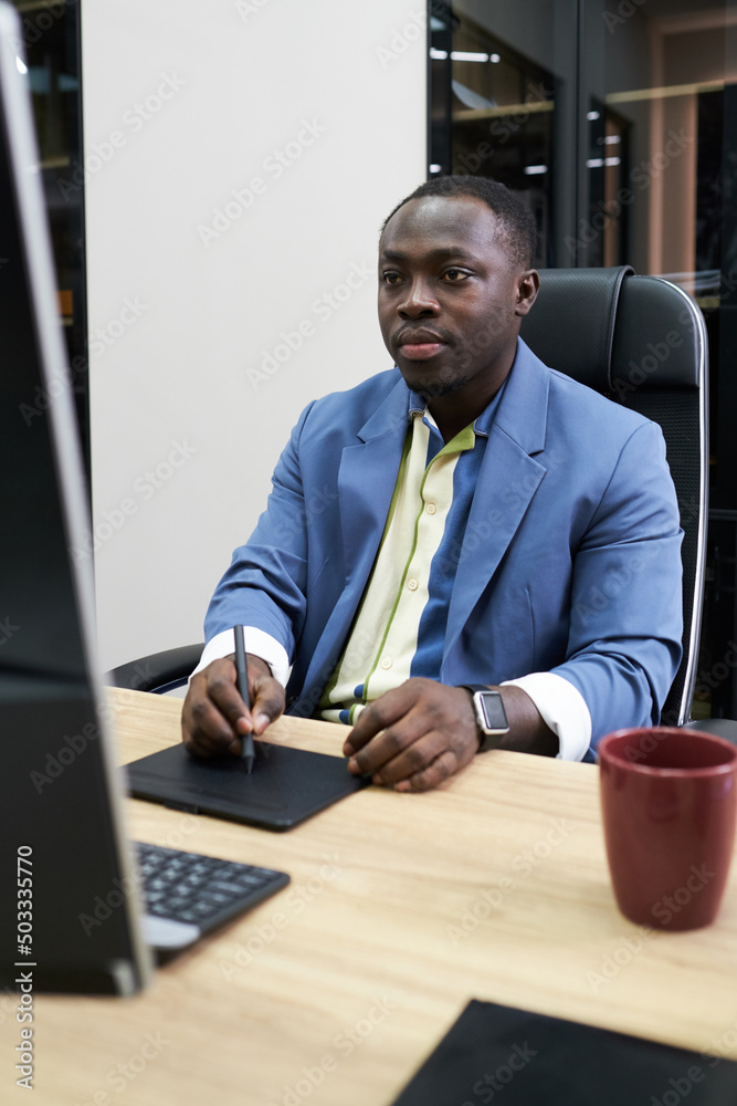 Poster african serious designer concentrating on his work at table with computer using graphic tablet
