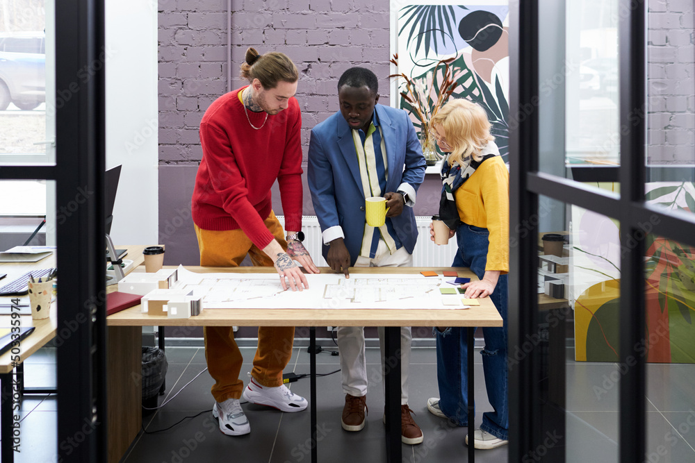 Poster Group of architects standing at table and working over blueprint in team, they discussing new construction project