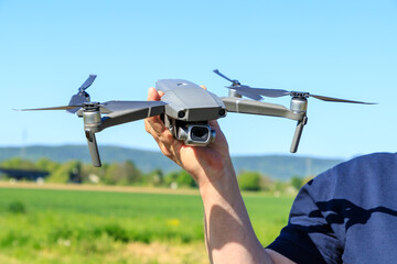 A man holding a drone in his hands before the start of the flight against the background of a field and blue sky.