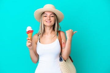 Young Romanian woman holding ice cream and beach bag isolated on blue background pointing to the side to present a product