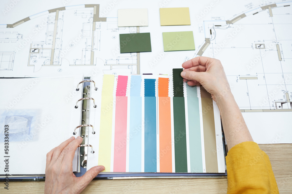 Poster close-up of interior designer choosing colour from colour palette while sitting at table with bluepr