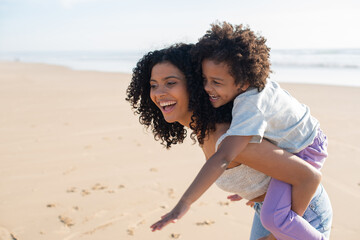 Content mother and daughter spending time on beach. African American family walking, laughing, playing, riding on back. Leisure, family time, parenthood concept